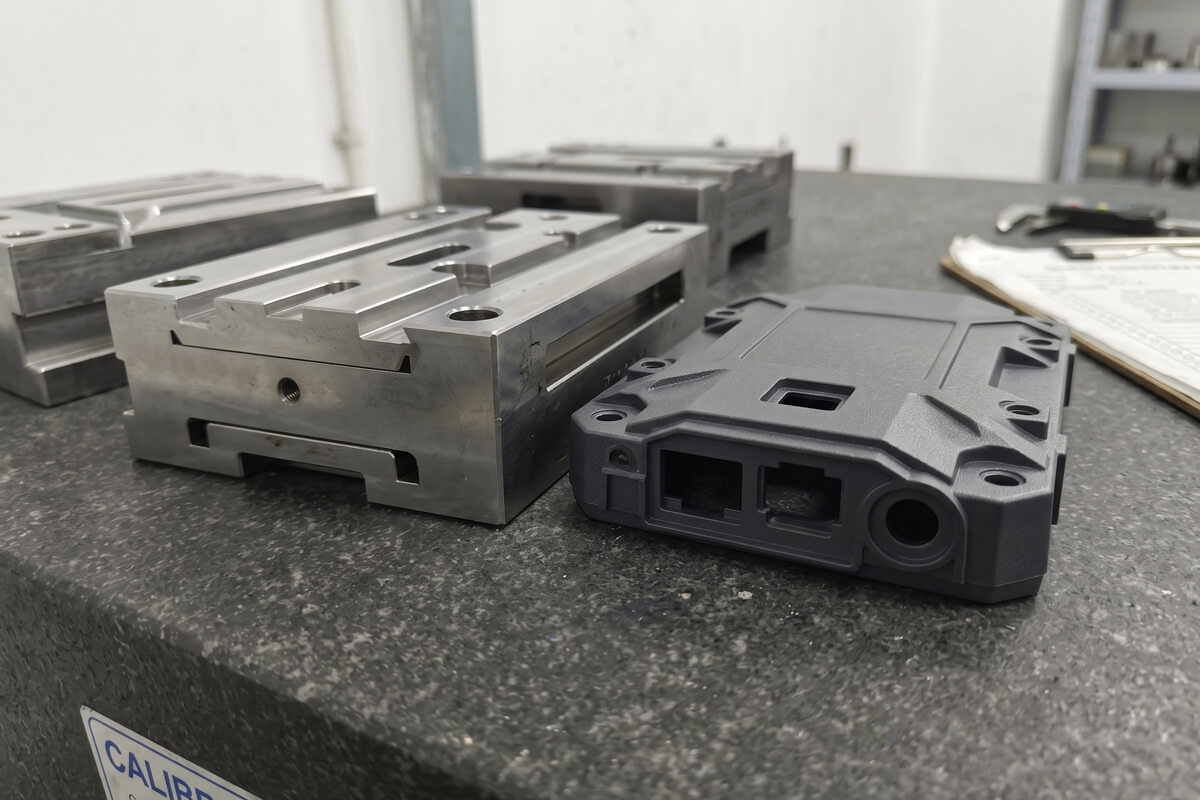 Macro view of a flash-free injection molded plastic enclosure next to its mating S136 wire EDM steel insert on a granite plate