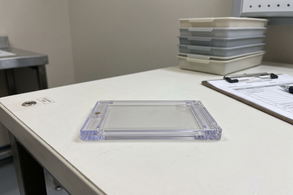 Transparent injection molded polycarbonate trading card protector case inspected on a cleanroom worktable