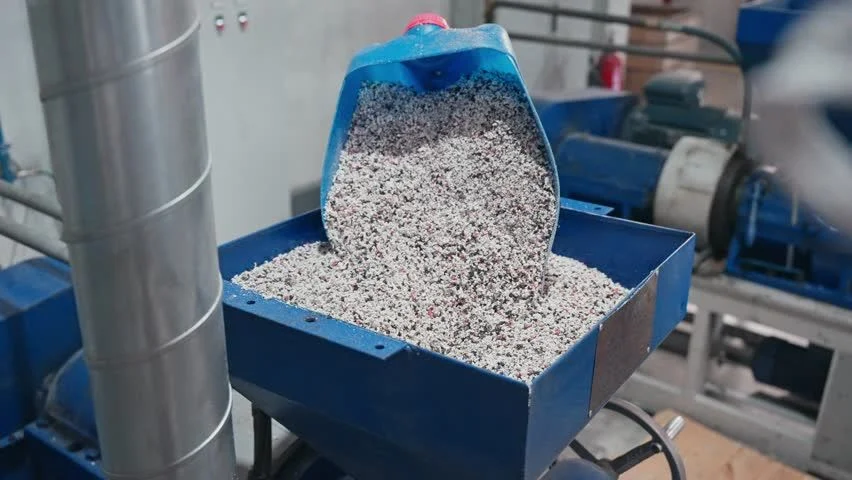 Plastic resin pellets being loaded into an injection molding machine hopper
