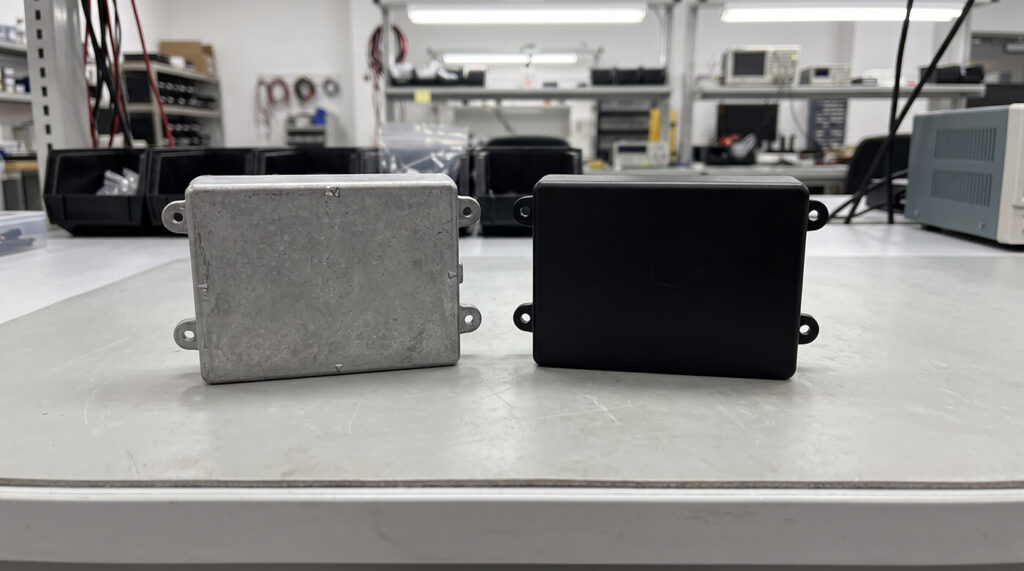 Aluminum die cast housing and plastic injection molded housing of similar shape side by side on a table