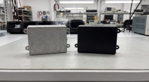 Aluminum die cast housing and plastic injection molded housing of similar shape side by side on a table