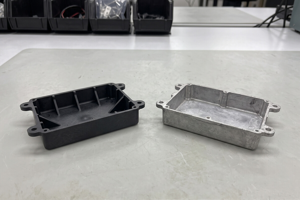 Glass-filled nylon bracket next to an aluminum die cast bracket on an inspection table