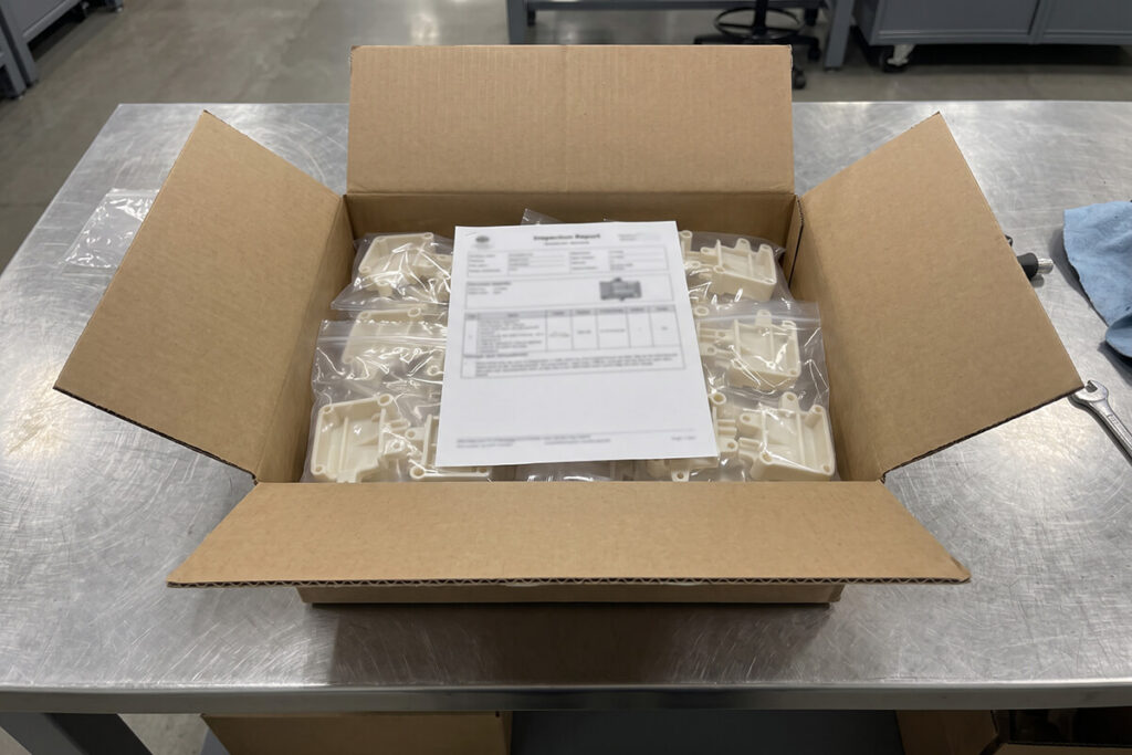 Carton of bagged molded parts with a printed inspection report resting on top