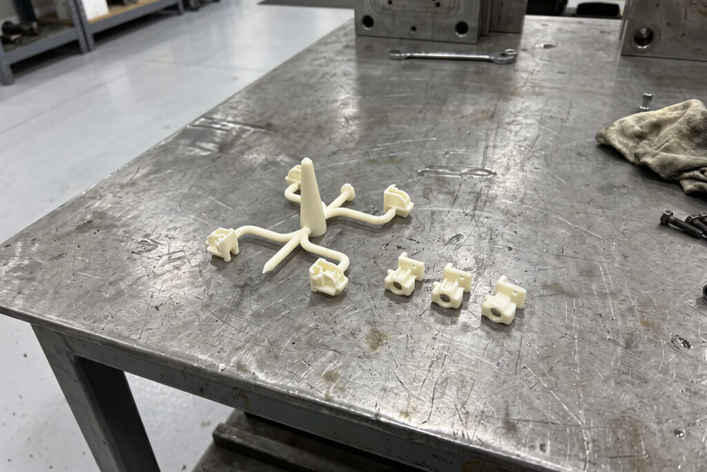Cold runner shot with parts attached to a branching runner and sprue next to loose finished parts