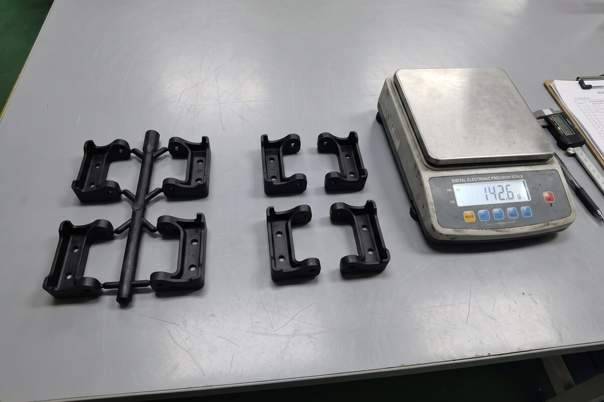 Side-by-side comparison of cold runner plastic parts attached to a thick sprue versus runnerless hot-runner molded parts on a scale