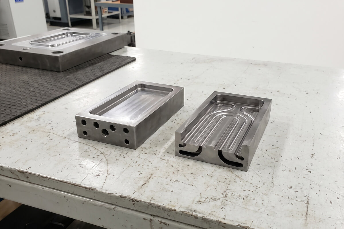 Two steel mold inserts side by side, one with straight drilled cooling channels and one with curved conformal cooling channels