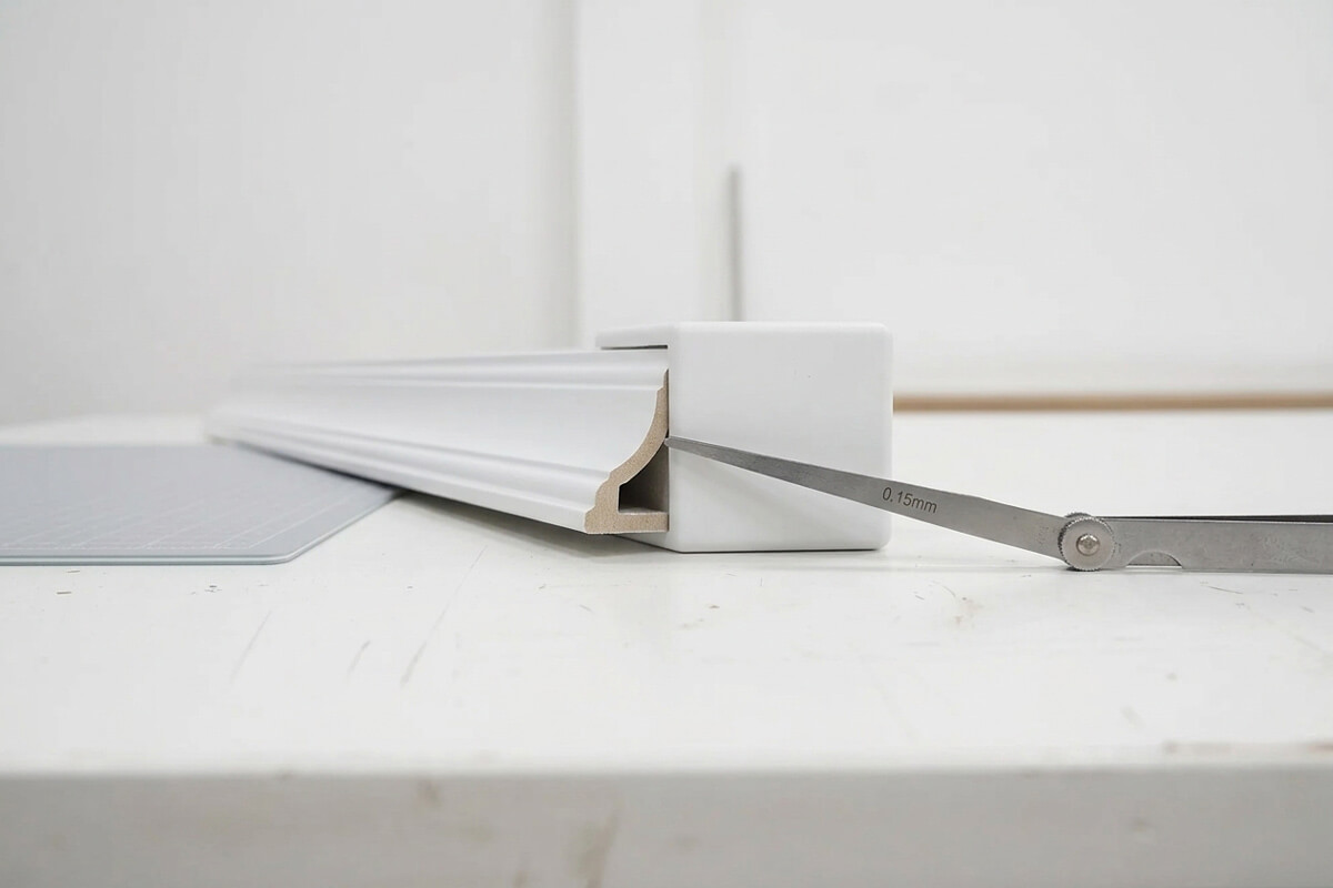 Extruded crown molding strip inserted into the socket of a molded corner block with a feeler gauge checking clearance