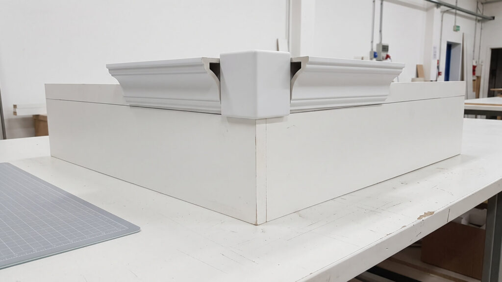 White crown molding strips meeting at a mock outside wall corner through an injection-molded corner block