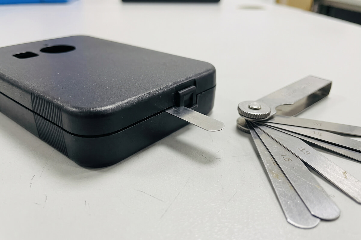 Feeler gauge blades checking the perimeter gap between a molded plastic lid and base during stack-up verification