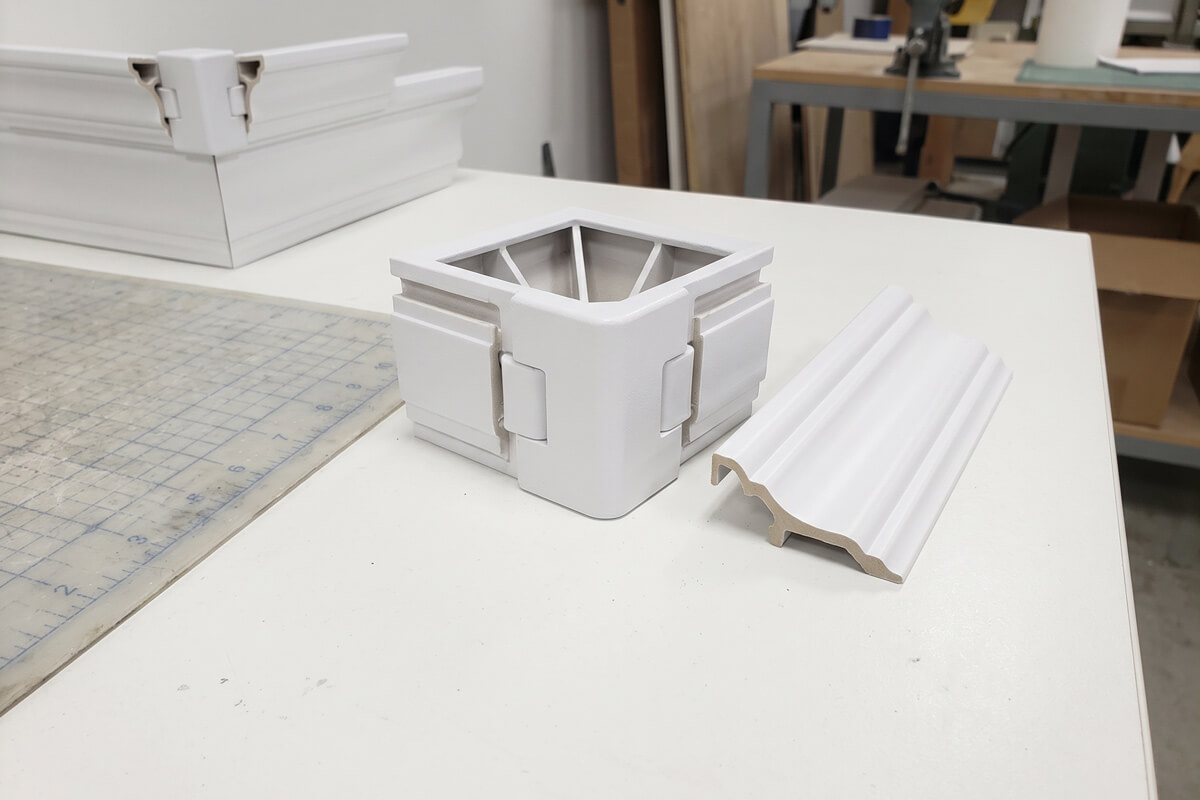 Close-up of a matte white injection-molded outside corner block for crown molding with two sockets and a hidden back parting line
