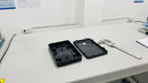Plastic enclosure base and lid on an inspection bench next to a digital caliper for injection molding tolerance checks
