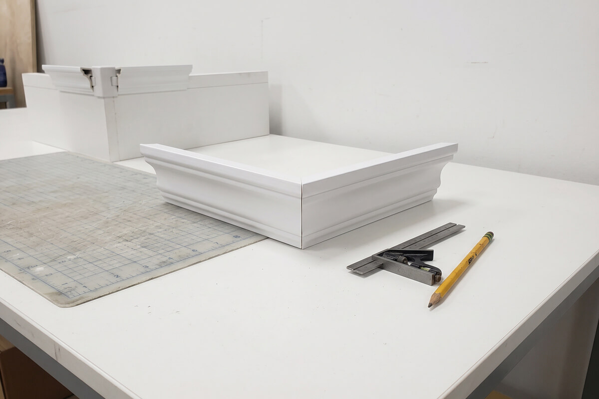 Two mitered plastic crown molding offcuts joined at an outside corner showing a visible gap at the miter joint