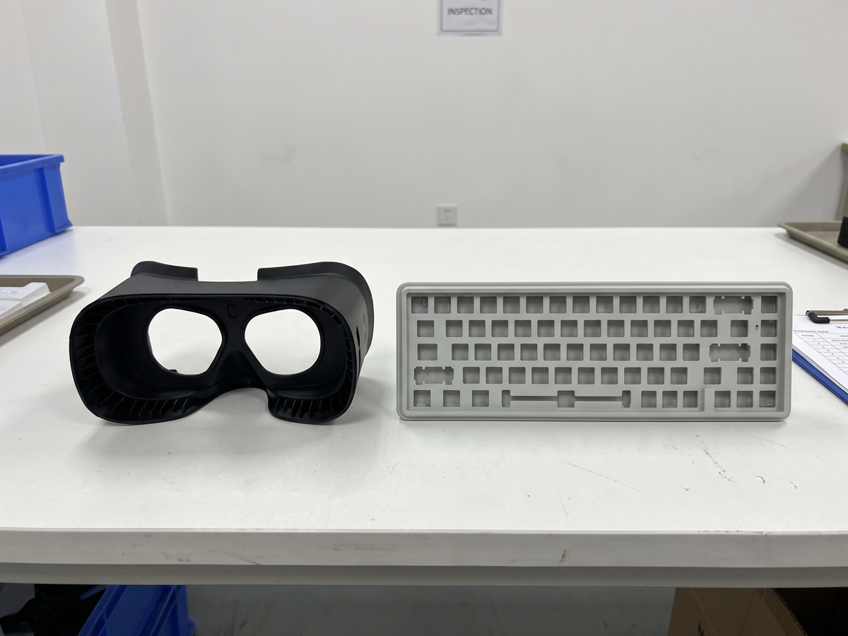 Injection molded industrial VR headset front shell and a low-profile mechanical keyboard top frame on a white inspection table