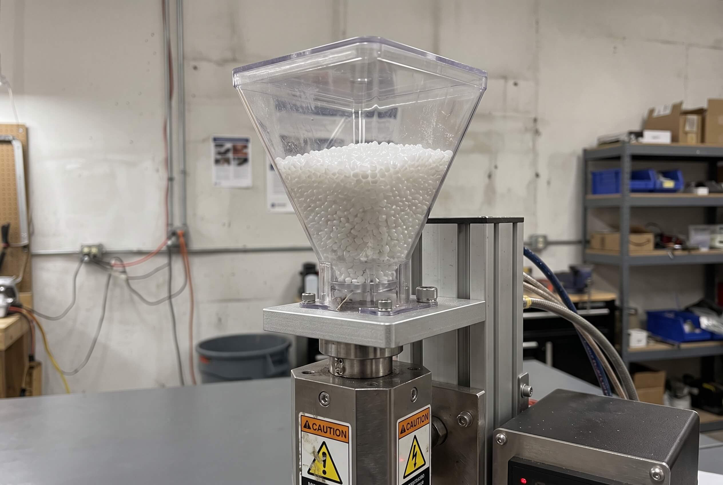 Close-up of a small resin pellet hopper loaded on a benchtop injection molding machine