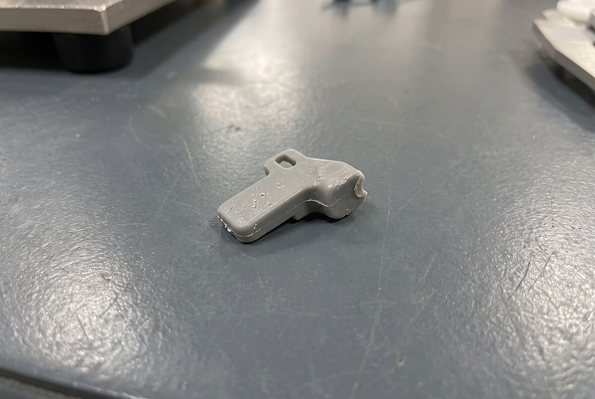 Small plastic part with a visible short-shot defect and rough surface finish on a worktable