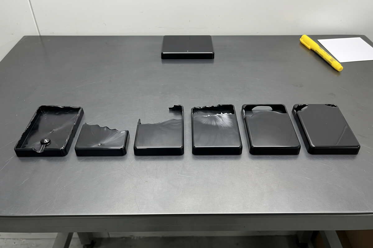 A row of six short-shot black lid parts filled to increasing levels, showing flow front progression