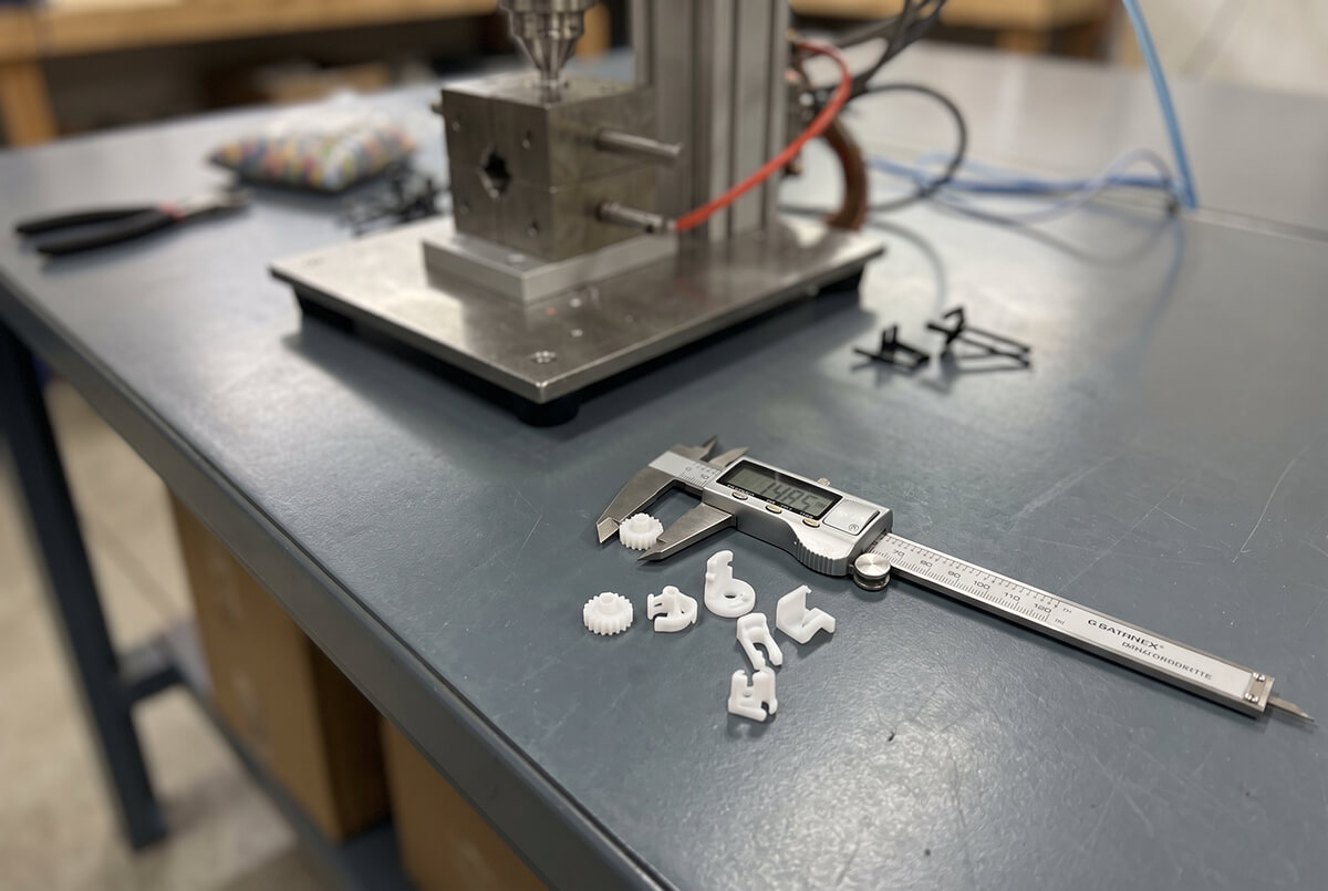 Small plastic prototype parts next to a digital caliper showing their scale
