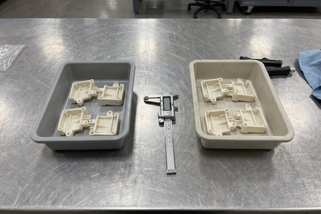 Two trays of identical molded sample parts with a digital caliper between them