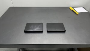 Two glossy black injection molded lid parts side by side, one with silver splay streaks near the gate and one clean